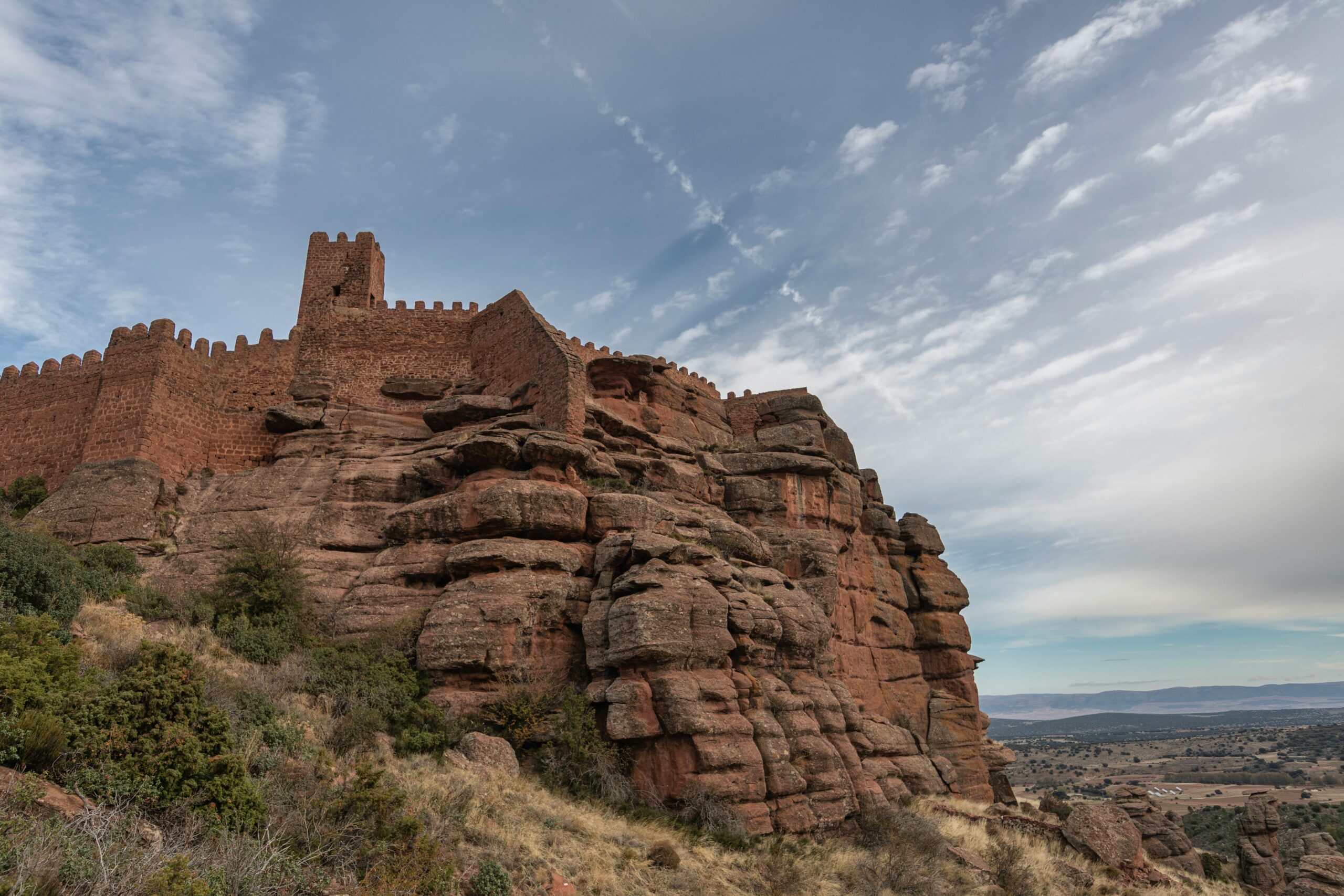 A stunning view of the Castle of Peracense perched on eroded rock formations under a vast sky.